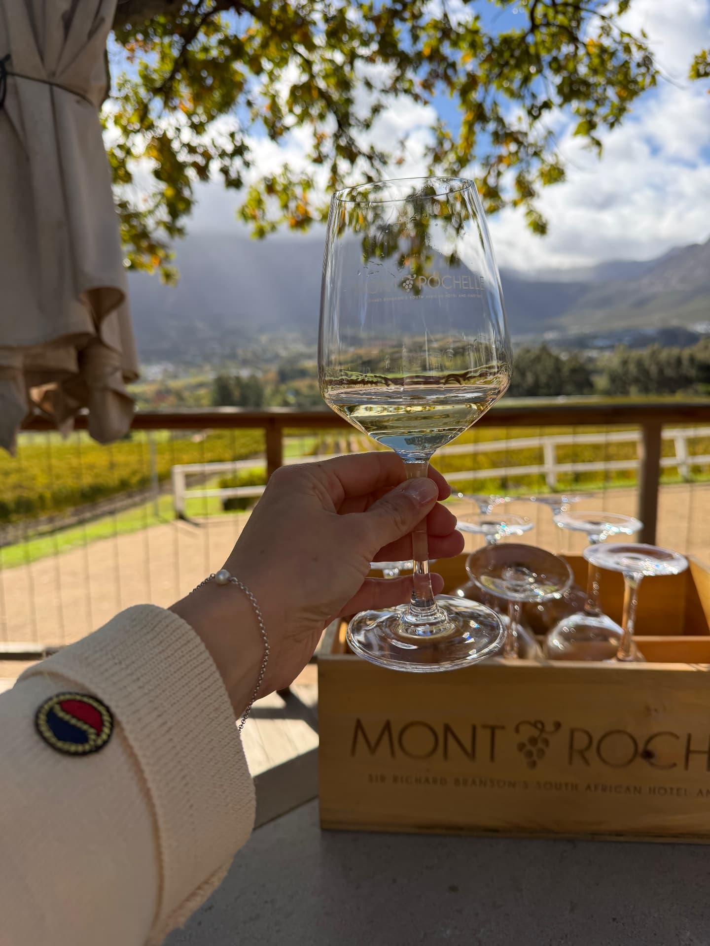 A glass of white wine held above the vineyards at Mont Rochelle, Franschhoek